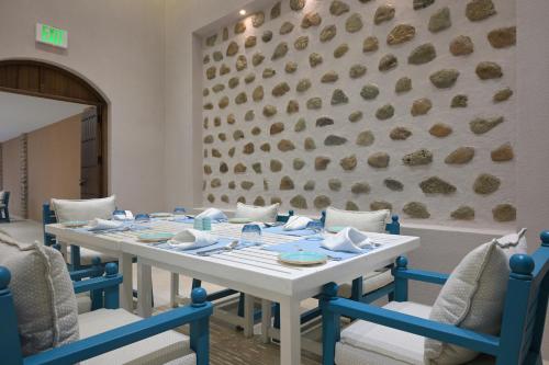 a white table with blue chairs and a wall with rocks at Nozol Al Rayaheen By Sharjah Collection in Khor Fakkan