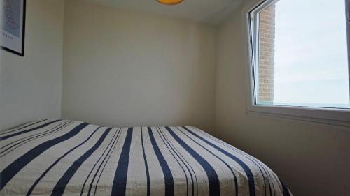 a bedroom with a striped bed and a window at l'Horizon de la digue - Vue mer in Bray-Dunes