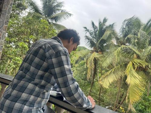a man standing on a fence looking at palm trees at Hippy Trail Guest House and Dorms in Arambol