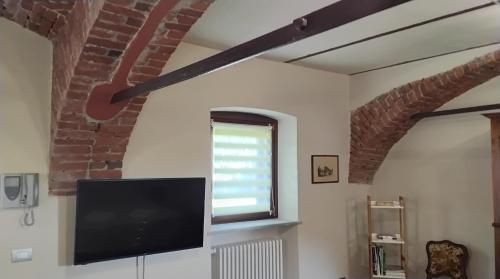 a living room with a tv and a brick wall at Cascina Tetto Cavallo Monolocale Rustico in Revello
