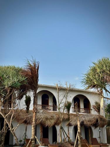 a house with a thatched roof and palm trees at The Beachbreaks Medewi in Airsatang