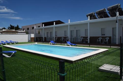 a swimming pool with chairs and a building at Alojamientos Alma in Conil de la Frontera