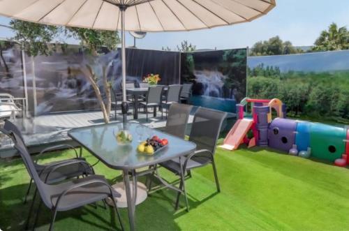eine Terrasse mit einem Tisch und Stühlen sowie einem Spielplatz in der Unterkunft Vila Granot - Boutique Villa in the Galilee in Shelomi