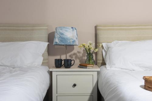 two beds with white sheets and a night stand with a lamp at Cape Cornwall Club in St. Just