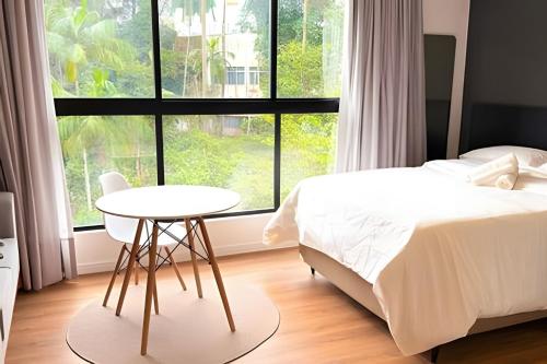 a bedroom with a bed and a table and a window at ASA | Loft UP ao Lado da FURB | Piscina + Oktober in Blumenau