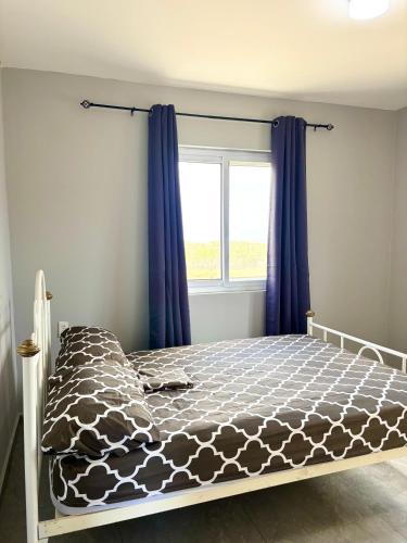 a bed in a bedroom with blue curtains and a window at 2BR Top Hill Island view and distant ocean view in Willemstad