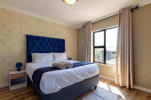 a bedroom with a bed with a blue headboard and a window at Alimamaspaces The Mansons Riverbend Midrand in Midrand