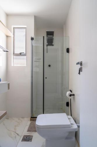 a white bathroom with a shower and a toilet at Elegante Ap | 3 Quartos c/Ar | 100m Praia do Forte in Škorak
