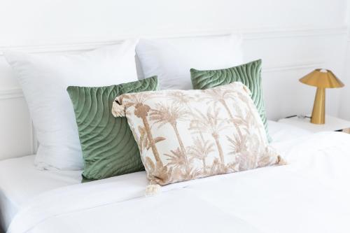 a white bed with green pillows and a palm tree pillow at L'Ecrin d'Or - Jacuzzi, Cinéma, 10 min gare à pied in Aulnay-sous-Bois