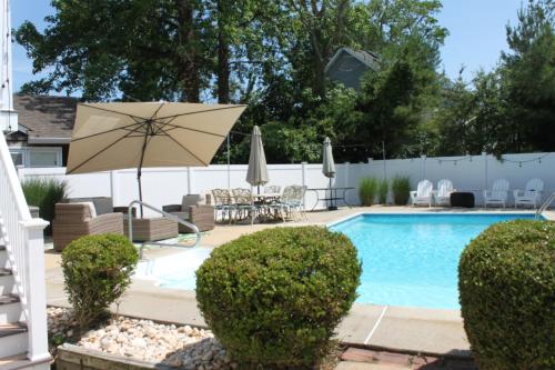 a swimming pool with an umbrella and chairs and a patio at Gorgeous beach house with large pool & private beach, just 3 blocks away!! in Point Pleasant Beach