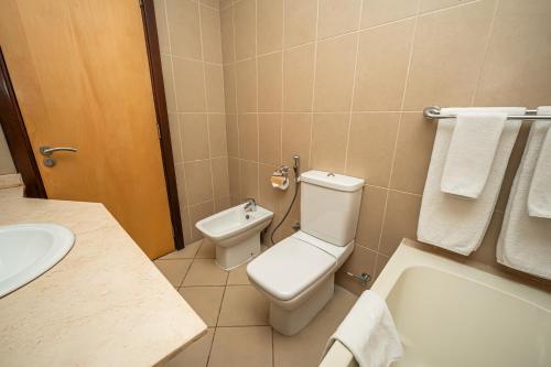 a bathroom with a toilet and a sink and a tub at Kingsgate Hotel Doha by Millennium Hotels in Doha