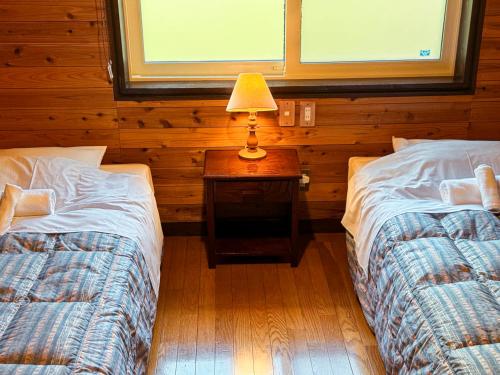a bedroom with two beds and a table with a lamp at Ringo Lodge Hakuba in Hakuba