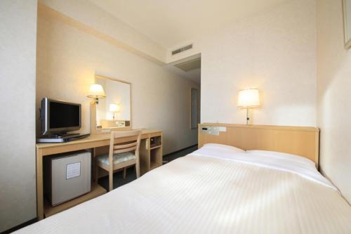 um quarto de hotel com uma cama e uma secretária com uma televisão em Kofu Washington Hotel Plaza em Kofu