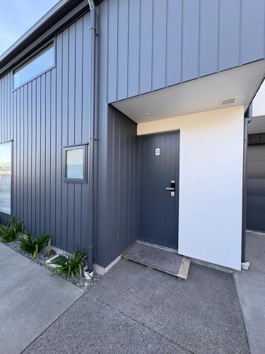 a gray building with a white door on it at Handy Riccarton New Home Walk to Westfield, Tower Junction & Close to Hagley Park in Christchurch