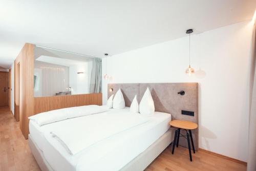 a white bedroom with a white bed and a table at Ganischgerhof Mountain Resort & Spa in Nova Ponente