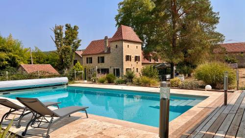 a swimming pool with two chairs next to a house at Ferme des Petites Oreilles 4 étoiles in Montignac