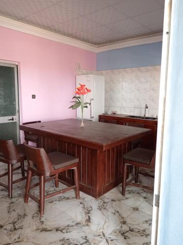 a kitchen with a large wooden table with chairs and a vase with a flower at Almar inter guest house in Porto-Novo