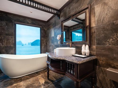 Un baño con bañera, lavabo y ventana. en Halong & Lan Ha Cruises, en Ha Long