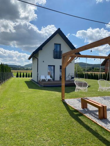 a small white house with a swing in the yard at Domek pod Sosnową Górą in Żelazno