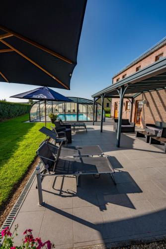 a group of lounge chairs and an umbrella on a patio at Logis Hôtel Le Menobu in Theux