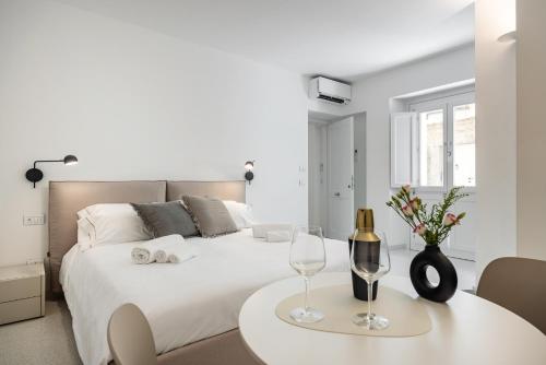 a white bedroom with a white bed and a table with wine glasses at Anita Rooms in Olbia