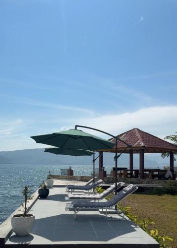 a group of lounge chairs and umbrellas next to the water at Hariara Guest House in Tuk Tuk