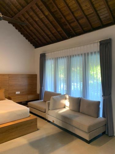 a bedroom with a bed and a couch next to a window at Lullaby Bungalows in Uluwatu