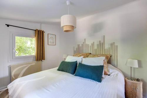 ein Schlafzimmer mit einem weißen Bett mit Kissen und einem Fenster in der Unterkunft Maison de vacances à Petit Piquey, entre Bassin et Océan in Lège-Cap-Ferret