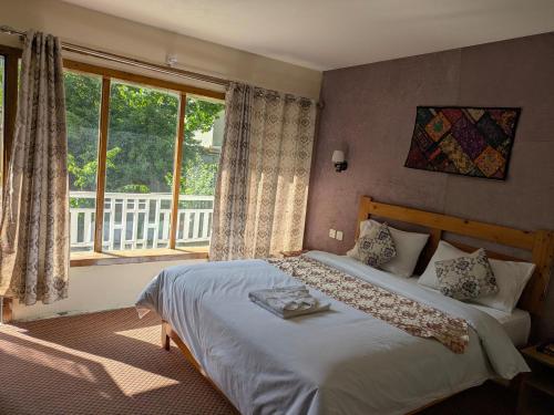 a bedroom with a bed and a large window at White Apricot Lodge in Baltit