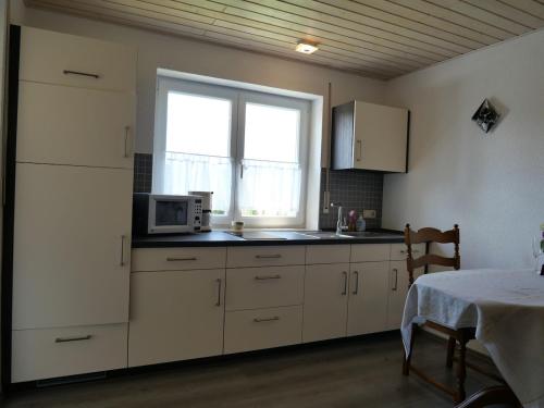 une cuisine avec des placards blancs, une fenêtre et une table dans l'établissement Ferienwohnung mit Entspannungserlebnis im Garten mit Terrasse, à Wildpoldsried