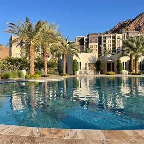 a large swimming pool with palm trees and a building at Flow - Al Raha Village in Aqaba