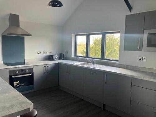a kitchen with white cabinets and a sink and a window at Stunning Contemporary Dutch Barn Conversion in Whixall