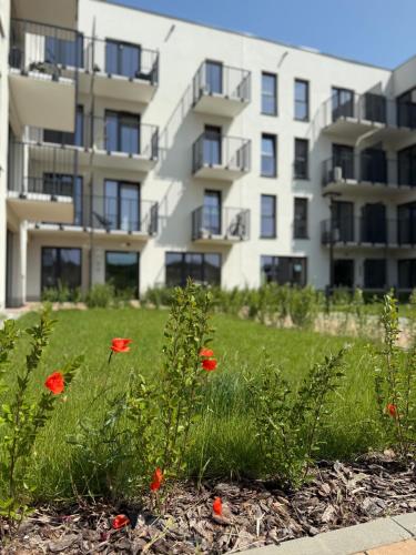 a apartment building with red flowers in the grass at CASHMERE Apartment - Airport Katowice-Pyrzowice in Siewierz