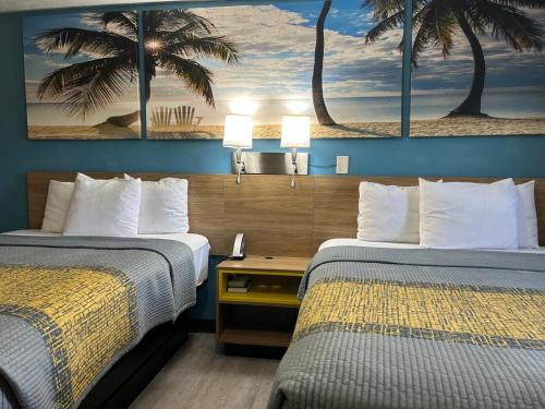 two beds in a hotel room with palm trees on the wall at Deerfield Inn in Parsons