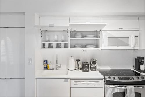 a white kitchen with a stove and a microwave at Spacious 3BR Condo w Patio & Skyline Views in Toronto