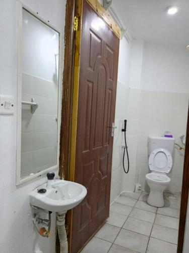 a bathroom with a sink and a toilet and a wooden door at Tulivu Studio 2nd Floor Apartment & Great Balcony View in Watamu