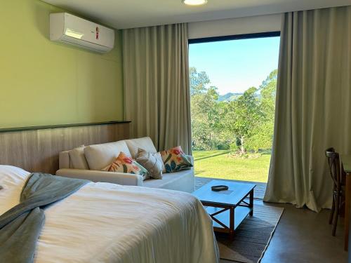 a bedroom with a bed and a couch and a window at Fazenda Boutique Vila dos Eucaliptos in Atibaia