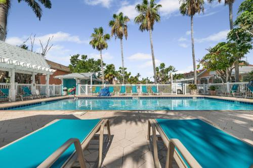 a swimming pool with chairs and palm trees at Barefoot Boho- Beach bungalow on Anna Maria Island in Bradenton Beach