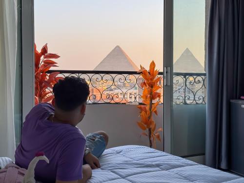a man sitting on a bed looking out a window at Giza pyramids view & jacuzii in Cairo