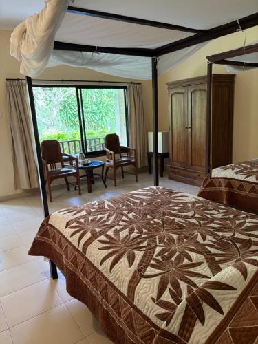 a bedroom with a bed and chairs and a large window at Raja Gardens Hotel in Seminyak