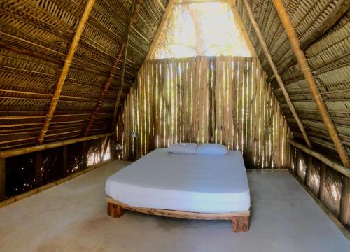 a bed in a thatched room with a mattress at Kin Resort Lodge in Maya Beach