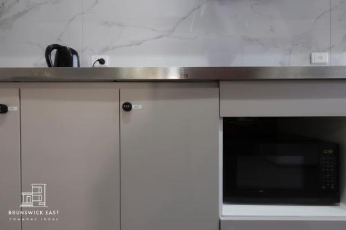 a kitchen with white cabinets and a microwave at 204 Stylish Twin BR with Fast WiFi - Brusnwick East in Melbourne