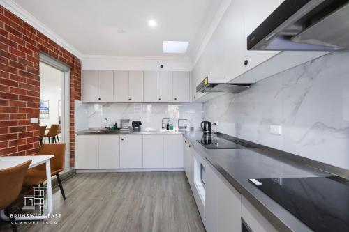 a kitchen with white cabinets and a brick wall at 205 Modern King BR with Fast WiFi - Brunswick East in Melbourne