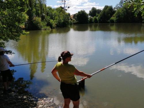 a woman is standing in the water holding a fishing pole at Chalet cosy - Vue sur l'étang avec terrasse - API-1-52-288 in Naucelle