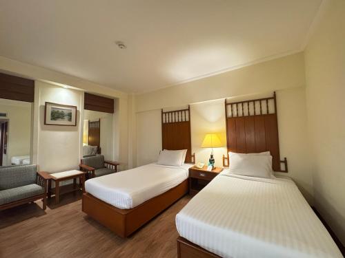 a hotel room with two beds and a chair at Bangkok Palace Hotel in Bangkok