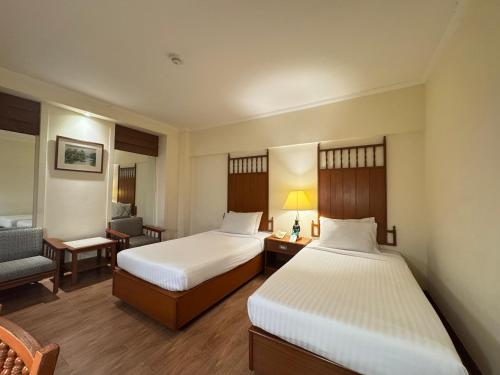 a hotel room with two beds and a chair at Bangkok Palace Hotel in Bangkok