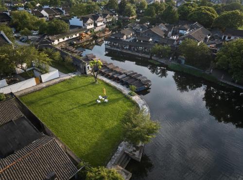 a person standing on a lawn next to a river at voco Xitang by IHG in Jiaxing