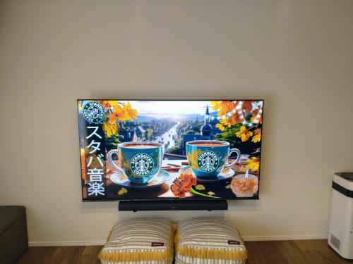 a flat screen tv hanging on a wall with two cups at Guest House Gifuhashima COCONE / Vacation STAY 30285 in Hashima