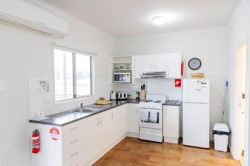 a kitchen with white cabinets and a white refrigerator at The Sundowner Cabin & Tourist Park in Whyalla