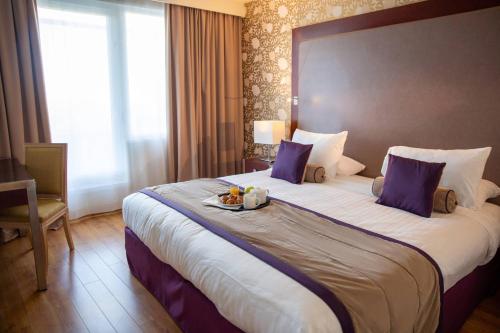 a hotel room with a large bed with a tray of food on it at Clarion Paris CDG Airport in Roissy-en-France
